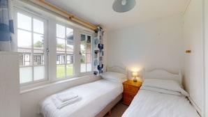 Une chambre avec deux lits simples, une table de chevet avec une lampe et une fenêtre avec des rideaux.