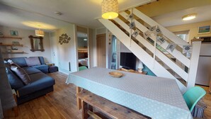 Une pièce chaleureuse avec un canapé, une table à manger, un banc en bois, un téléviseur et un escalier.