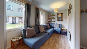 Un salon chaleureux avec un canapé d’angle, une petite table en bois et une fenêtre avec des rideaux.