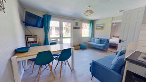 Un espacio habitable compacto con una mesa de comedor, sillas, un sofá, un televisor y una kitchenette.