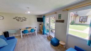 A room with a dining table, chairs, a sofa, a TV, and a large window with a view of the outside. - 31 Trevithick Court, Tolroy Manor (Hayle)