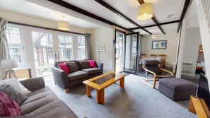 Ein modernes Wohnzimmer mit Sofa, Sessel und Couchtisch. Es gibt einen Essbereich mit Tisch und Stühlen. Das Zimmer verfügt über große Fenster und einen Ausblick nach draußen.