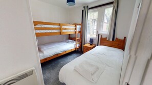 Ein Zimmer mit Etagenbetten, einem Einzelbett, einem Nachttisch mit Lampe und einem fenster mit Vorhängen.