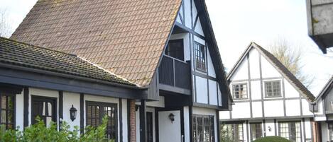 A traditional half-timbered house with a steeply pitched roof and a small garden area with a bench and a table.