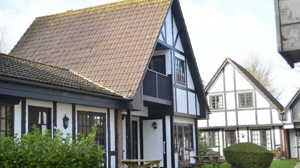 A traditional half-timbered house with a steeply pitched roof and a small garden area with a bench and a table.