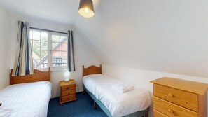 Ein Schlafzimmer mit zwei Einzelbetten, einer Holzkommode, einem Nachttisch mit Lampe und einem Fenster mit Vorhängen.
