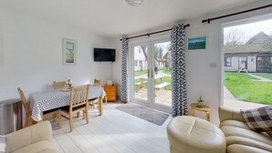 A room with a dining table, chairs, a sofa, a TV, and a sliding glass door leading to an outdoor area. - 25 Trevithick Court, Tolroy Manor (Hayle)