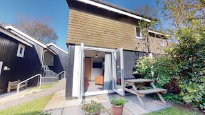 A wooden house with a sliding glass door leading to a patio area.