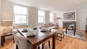 A modern living room with a dining area, large windows, a fireplace, and a painting on the wall.