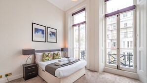 A bedroom with a bed, nightstand, lamp, and two framed pictures on the wall.