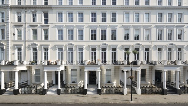 A row of white townhouses with symmetrical windows, a central entrance, and a balcony on the second floor.