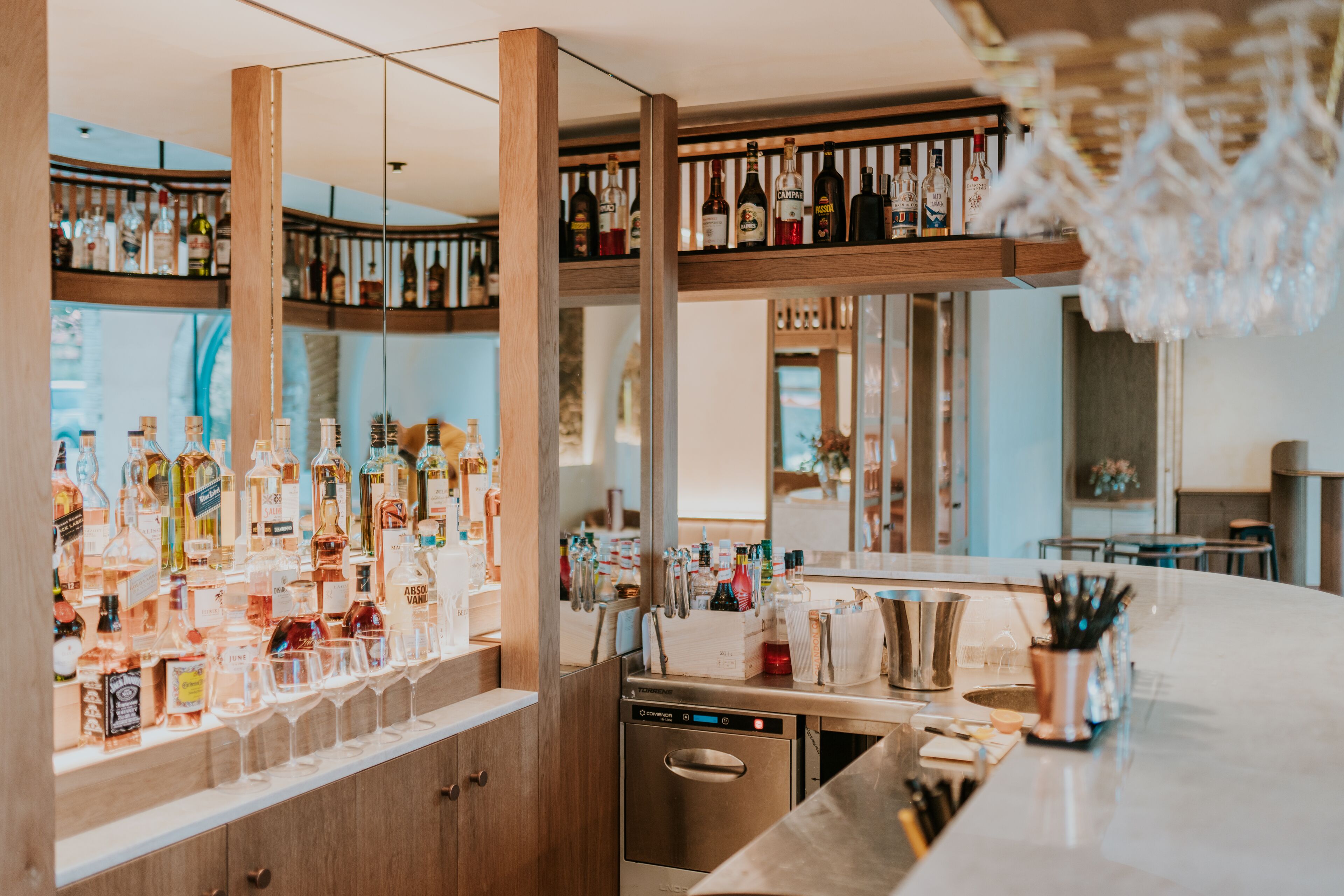 Een barruimte met flessenkast, vaatwasser en een bar met glazen en bestek.