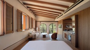 A modern hotel room with a large bed, a sofa, a coffee table, and a view of the outdoors through large windows. - Gran Hotel Mas d' en Bruno (Torroja del Priorat)