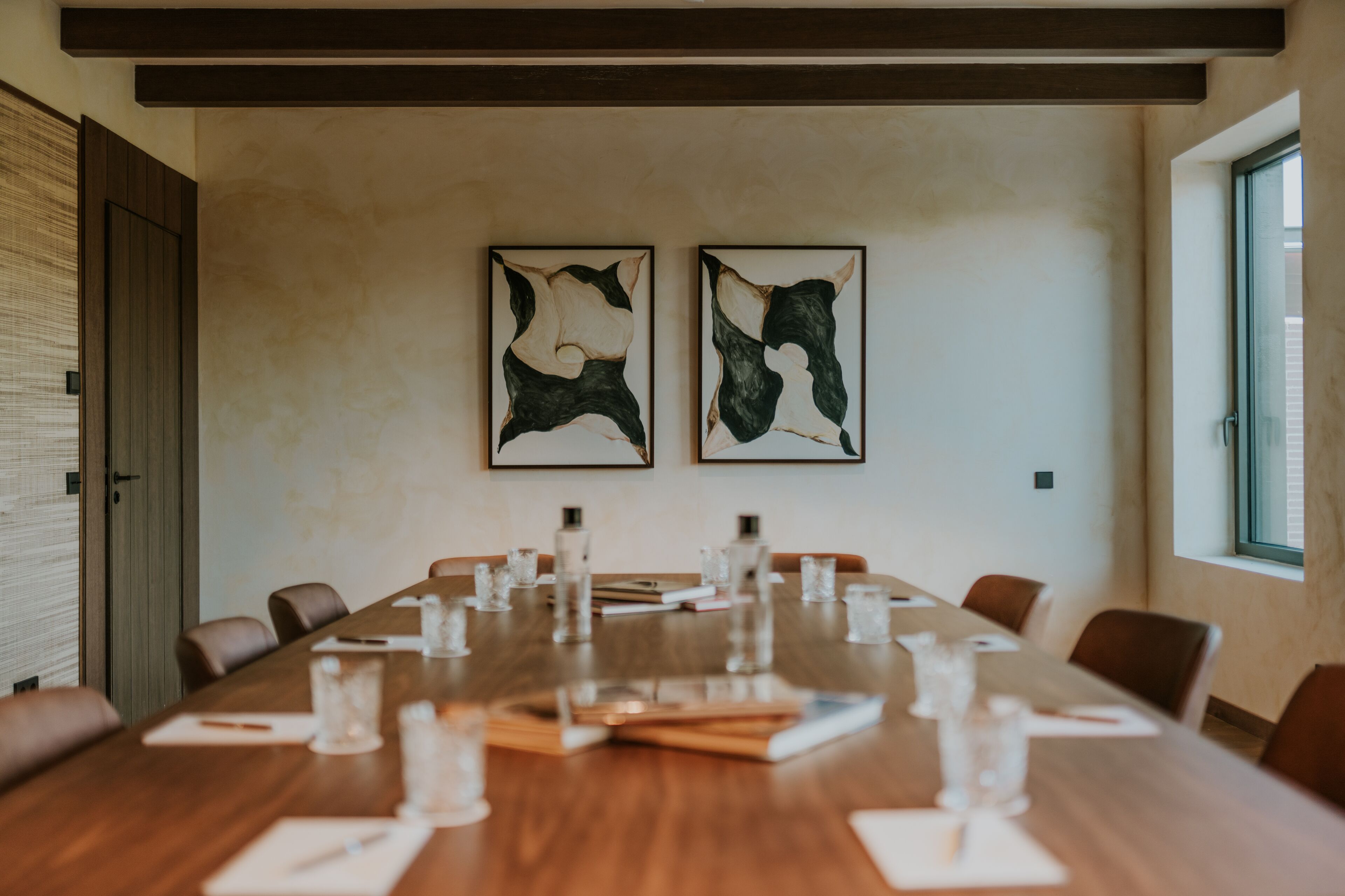 Un salón de conferencias con una larga mesa de madera, sillas y dos cuadros abstractos en la pared.