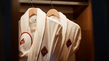 Three white robes hanging on wooden hangers in a closet.
