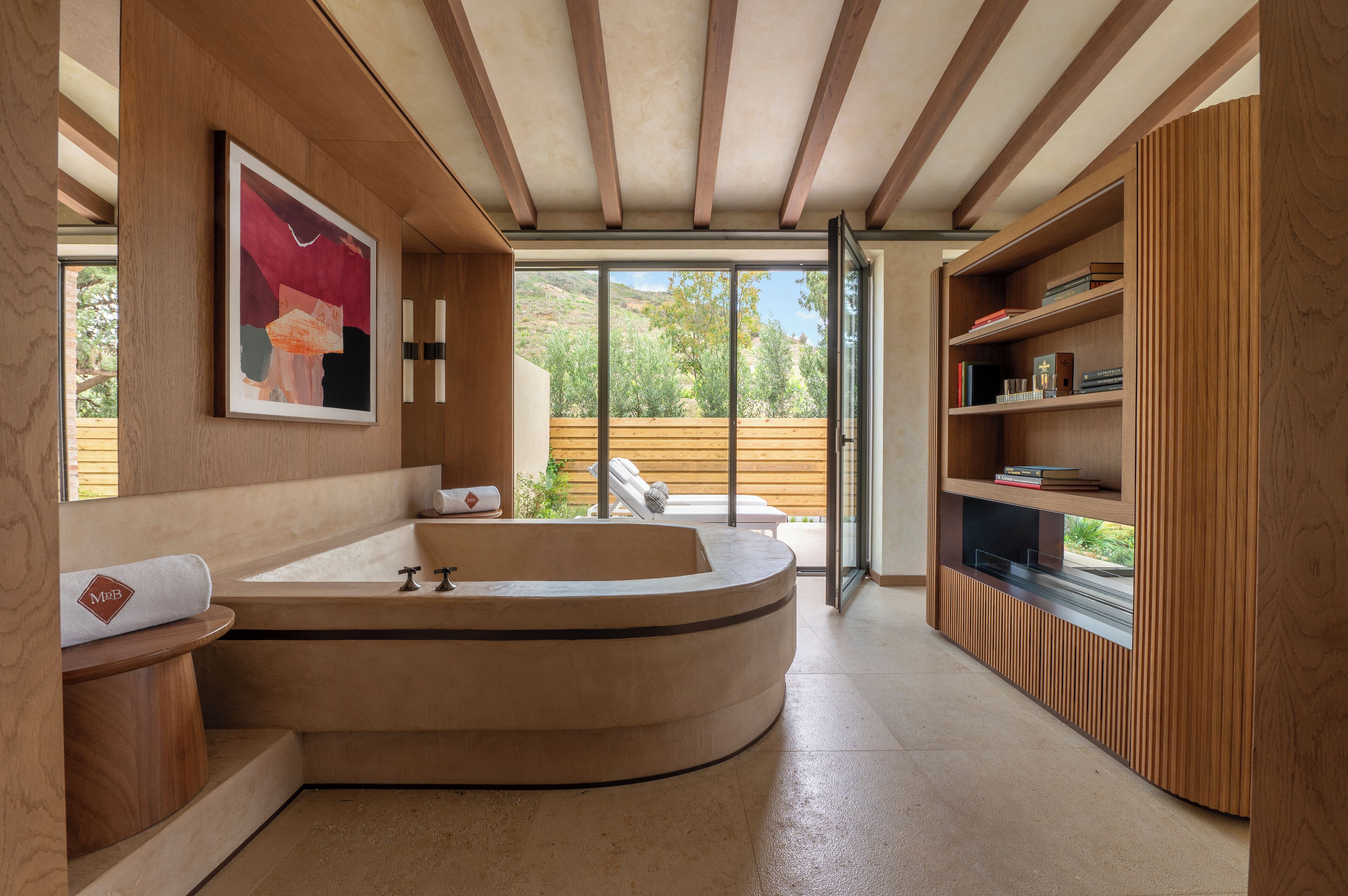 Un baño moderno con una bañera independiente, estanterías de madera y un amplio ventanal con vistas al exterior.