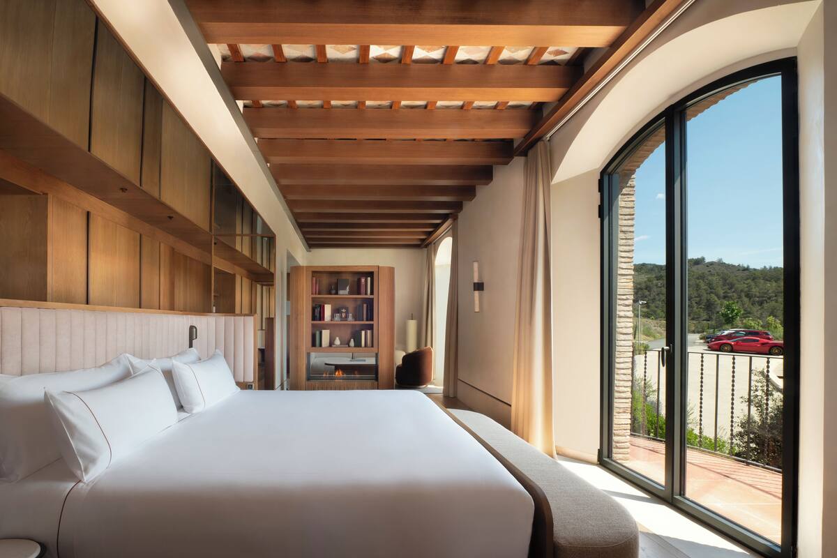 A modern hotel room with a large bed, built-in bookshelves, and a balcony with a scenic view.
