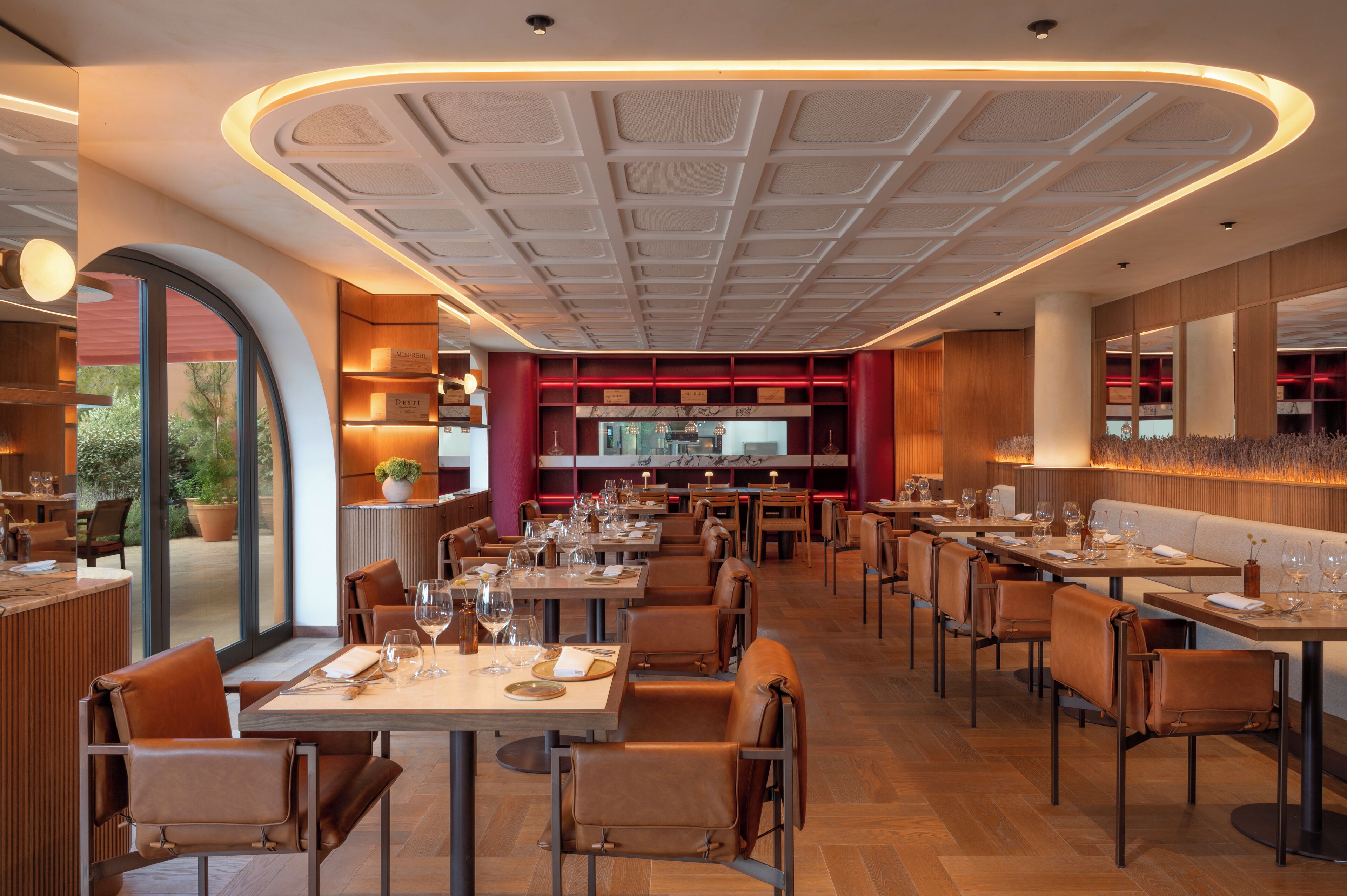 A modern restaurant with a central open dining area, multiple tables, and a view of the outdoors.