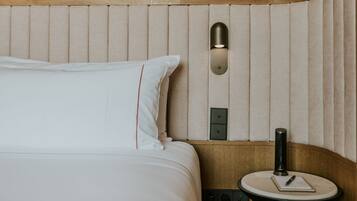 A neatly made bed with a pillow, a bedside table with a lamp, and a wall-mounted light fixture.
