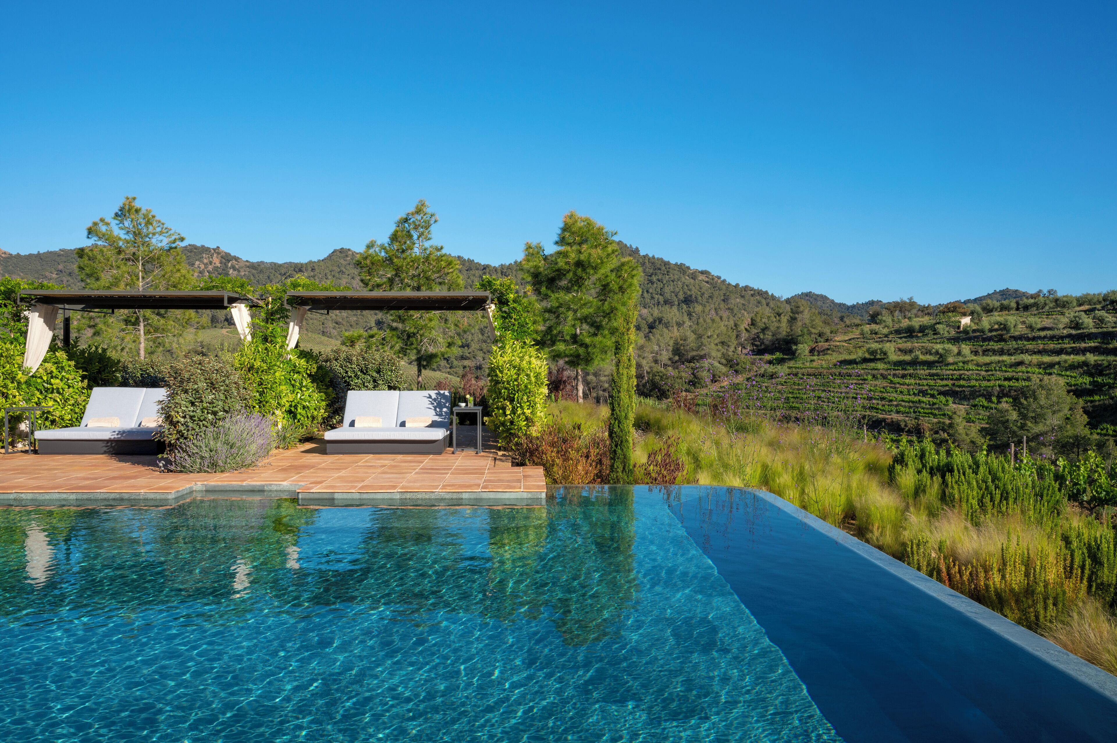 An infinity pool with clear blue water, surrounded by lounge chairs and a pergola.