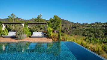 An infinity pool with clear blue water, surrounded by lounge chairs and a pergola.