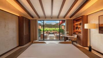 A modern hotel room with a large bed, a view of a garden and mountains, and a cozy seating area with a table and chairs.