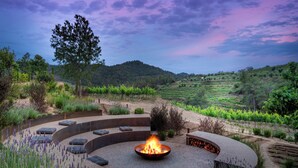 A circular outdoor seating area with a fire pit, surrounded by gravel and plants, overlooking a vineyard. - Gran Hotel Mas d' en Bruno (Torroja del Priorat)