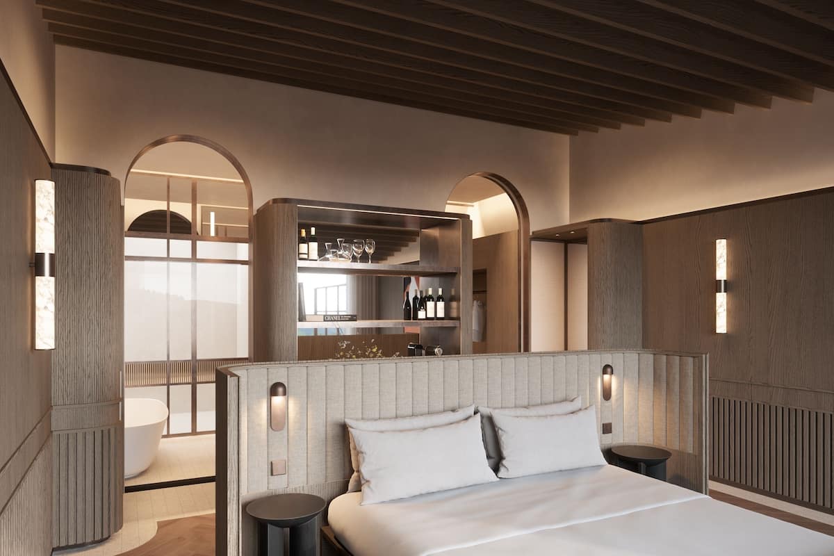 A modern hotel room with a large bed, a built-in minibar, and a view through an arched doorway.