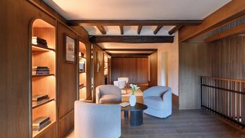 A modern interior with a wooden bookshelf, two armchairs, a small table, and a vase with flowers.