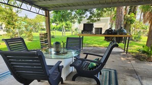 Eine überdachte Terrasse mit einem Glastisch, schwarzen Stühlen, einem Grill und einer Laterne.