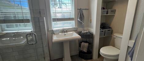 Ein Badezimmer mit Badewanne, Waschbecken und Toilette. Körbe und Regale mit Toilettenartikeln sind vorhanden.