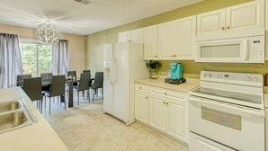 A kitchen with white cabinets, a microwave, an oven, and a dining area with chairs and a table. - Groups, Family, Graduation, Fort Jackson, USC Downtown (Columbia)