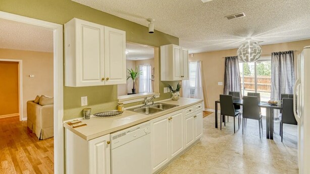 A kitchen with white cabinets, a sink, and a dining area with a table and chairs. - Groups, Family, Graduation, Fort Jackson, USC Downtown (Columbia)