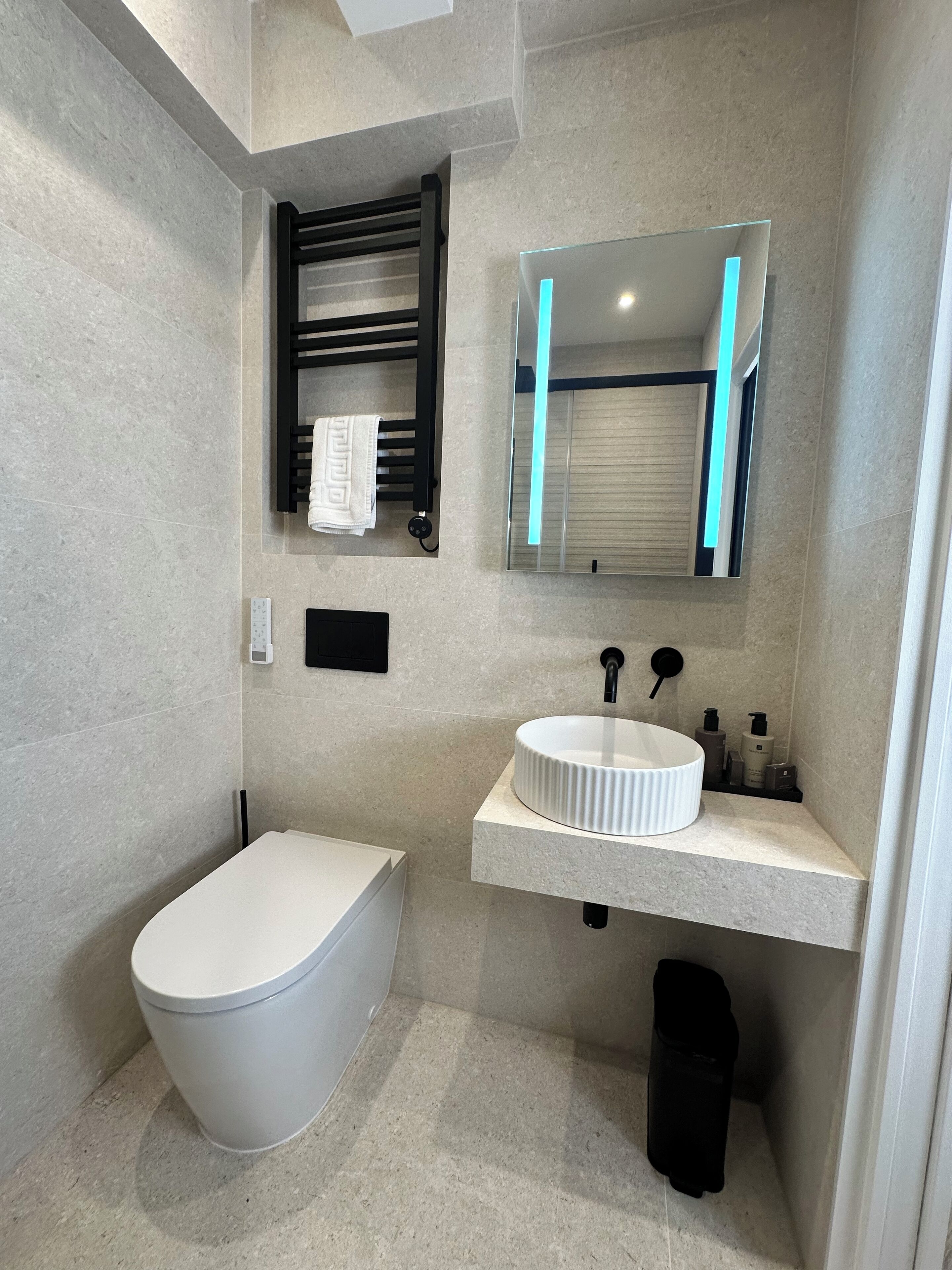 Ein modernes Badezimmer mit Toilette in Weiß, einem runden Waschbecken und einem Spiegel mit schwarzem Rahmen.