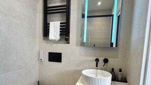 Un baño moderno con inodoro blanco, un lavabo redondo y un espejo con marco negro.