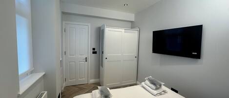 A hotel room with a bed, two white doors, a TV mounted on the wall, and a window.