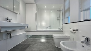 A modern bathroom with a large mirror, a bathtub, a toilet, and a bidet. - Chiltern Street Apartments - Superior E (London)