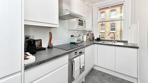 Una cucina moderna con mobili bianchi, forno a microonde integrato, piano cottura a gas e una finestra vista su un edificio in mattoni.