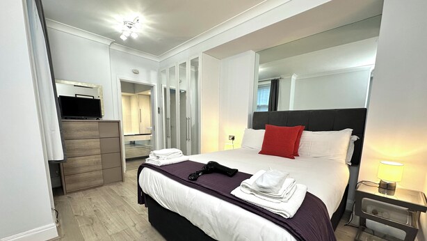 Une chambre d’hôtel moderne dotée d’un grand lit, d’une télévision, d’une armoire et d’une salle de bain visible à travers une porte en verre.