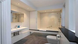 A modern bathroom with a large bathtub, a separate shower area, and a vanity with a mirror.