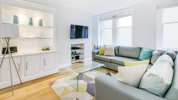 A modern living room with a grey sofa, a glass coffee table, and a TV mounted on the wall.