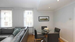 A modern living room with a glass dining table, black chairs, a grey sofa, and a framed picture on the wall.