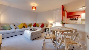 A modern living room with a sofa, ottoman, and a dining area with a table and chairs.
