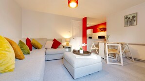 A modern living room with a grey sofa, colorful cushions, a wooden side table, and a red accent wall.