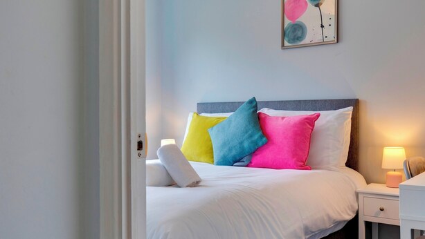 A neatly made bed with colorful pillows, a bedside lamp, and a wall art piece above it.