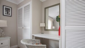 A bedroom with a white wardrobe, a bedside table with a lamp, a wicker chair, a desk with a mirror, and a red vase with flowers. - Stylish 2 Bedroom Flat Apartment with Free Parking in Windsor - Pass the Keys (Windsor)