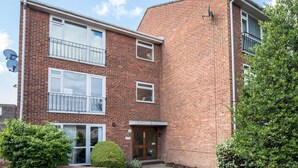 A two-story brick apartment building with a front entrance, satellite dishes, and a small garden area. - Stylish 2 Bedroom Flat Apartment with Free Parking in Windsor - Pass the Keys (Windsor)