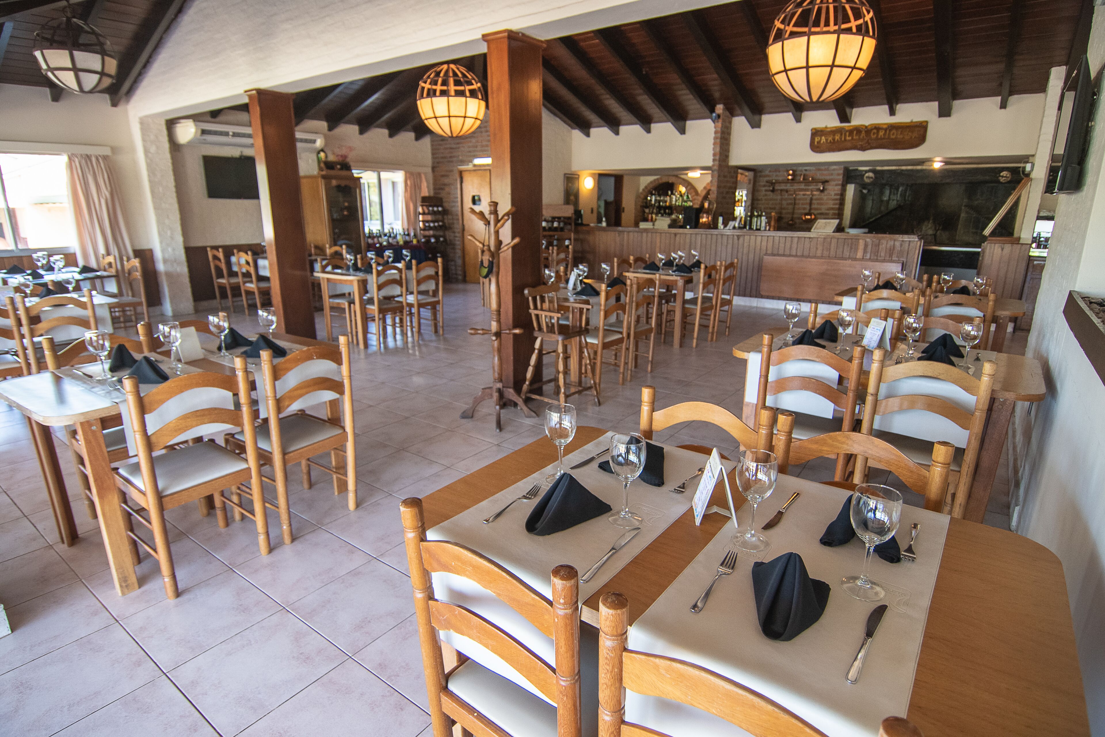 A restaurant with wooden tables and chairs, a bar area, and a brick wall.