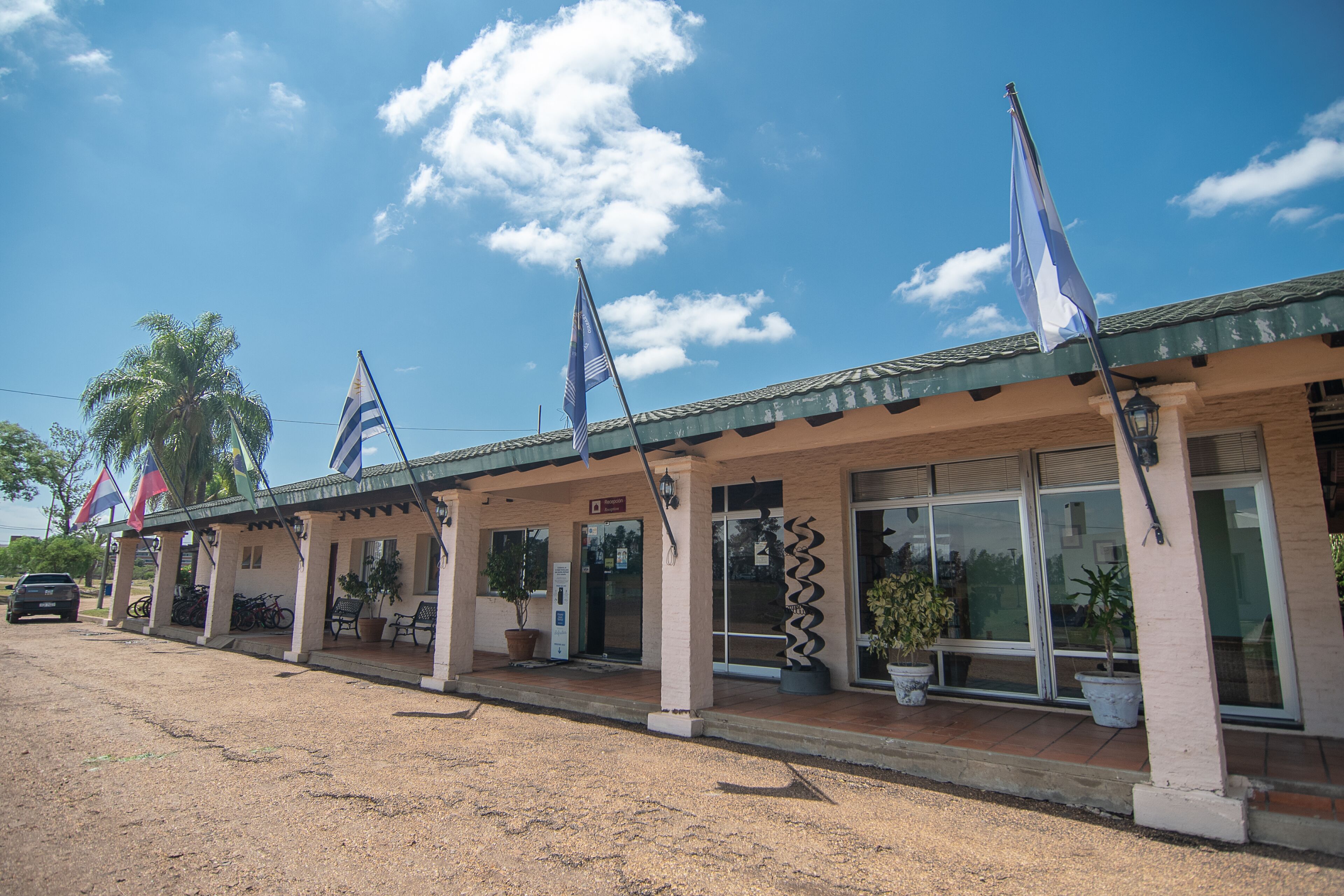 A building with multiple flags, a covered entrance, and potted plants.