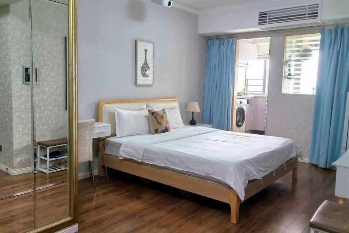Un dormitorio con cama de madera, mesita de noche, espejo y ventana con cortinas.